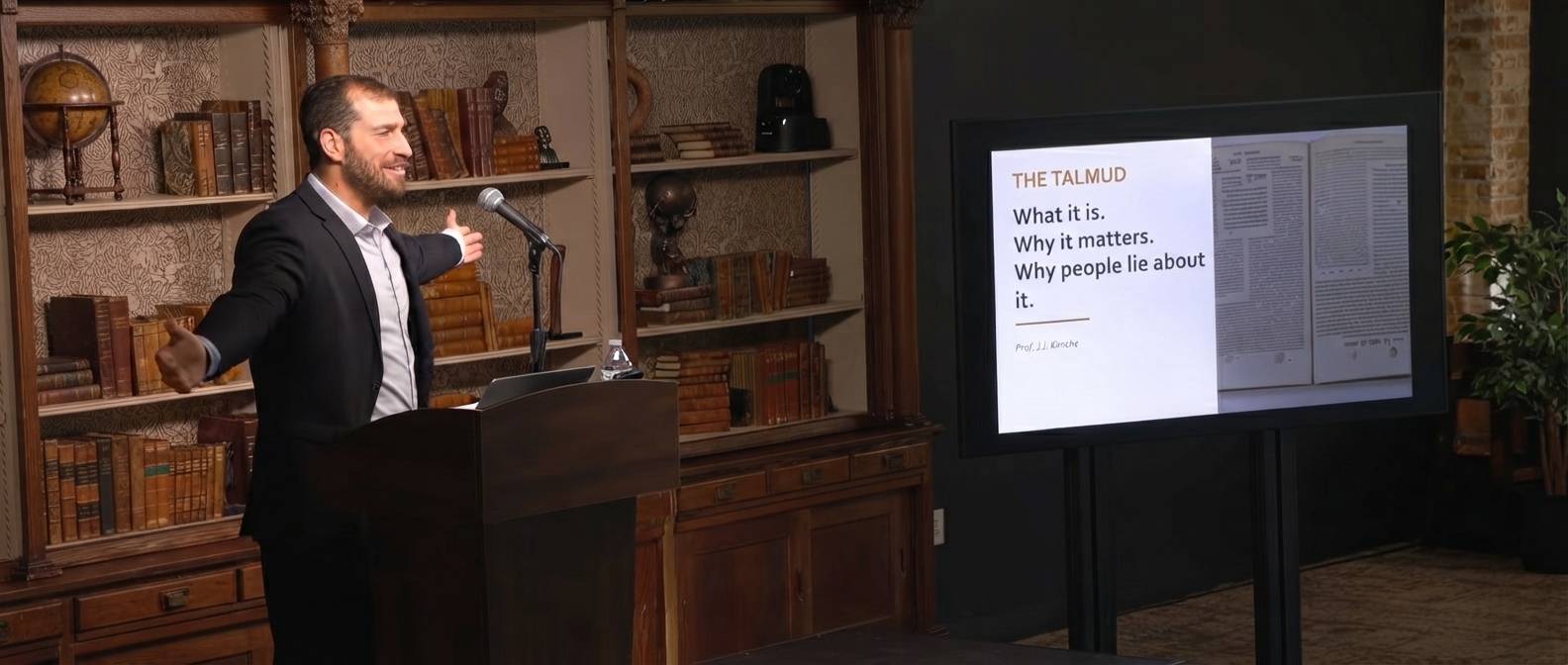J.J. Kimche lecturing at a lectern, with a presentation slide on the Talmud displayed behind him